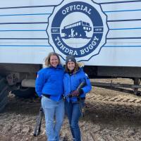 two women in blue coats standing in front of tundra buggy